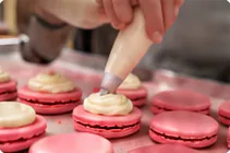 Cream being piped onto pink macaron shells